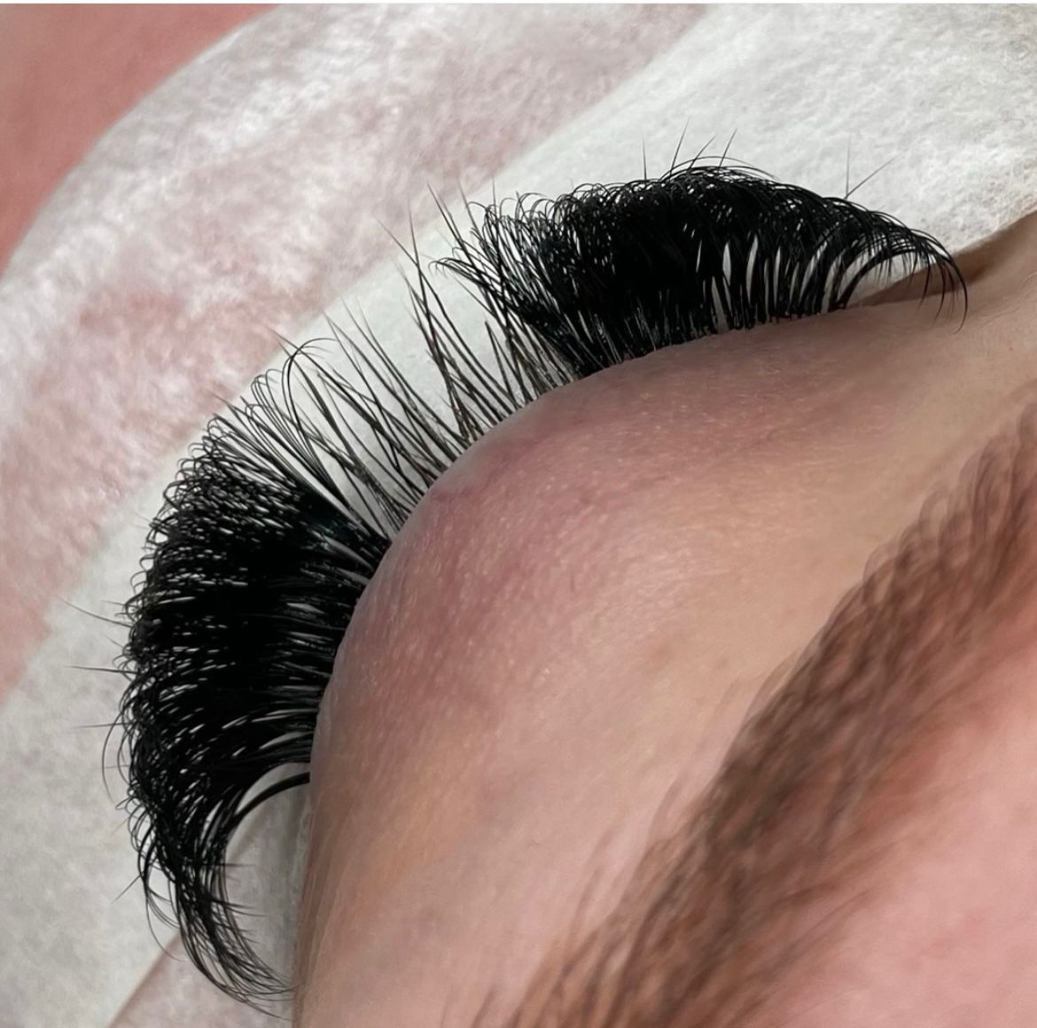 Nahaufnahme eines geschlossenen Auges mit langen schwarzen Wimpern und einer sichtbaren Augenbraue.