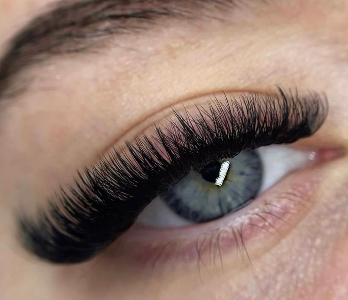 Nahaufnahme eines menschlichen Auges mit langen, dichten schwarzen Wimpern und blaugrauer Iris