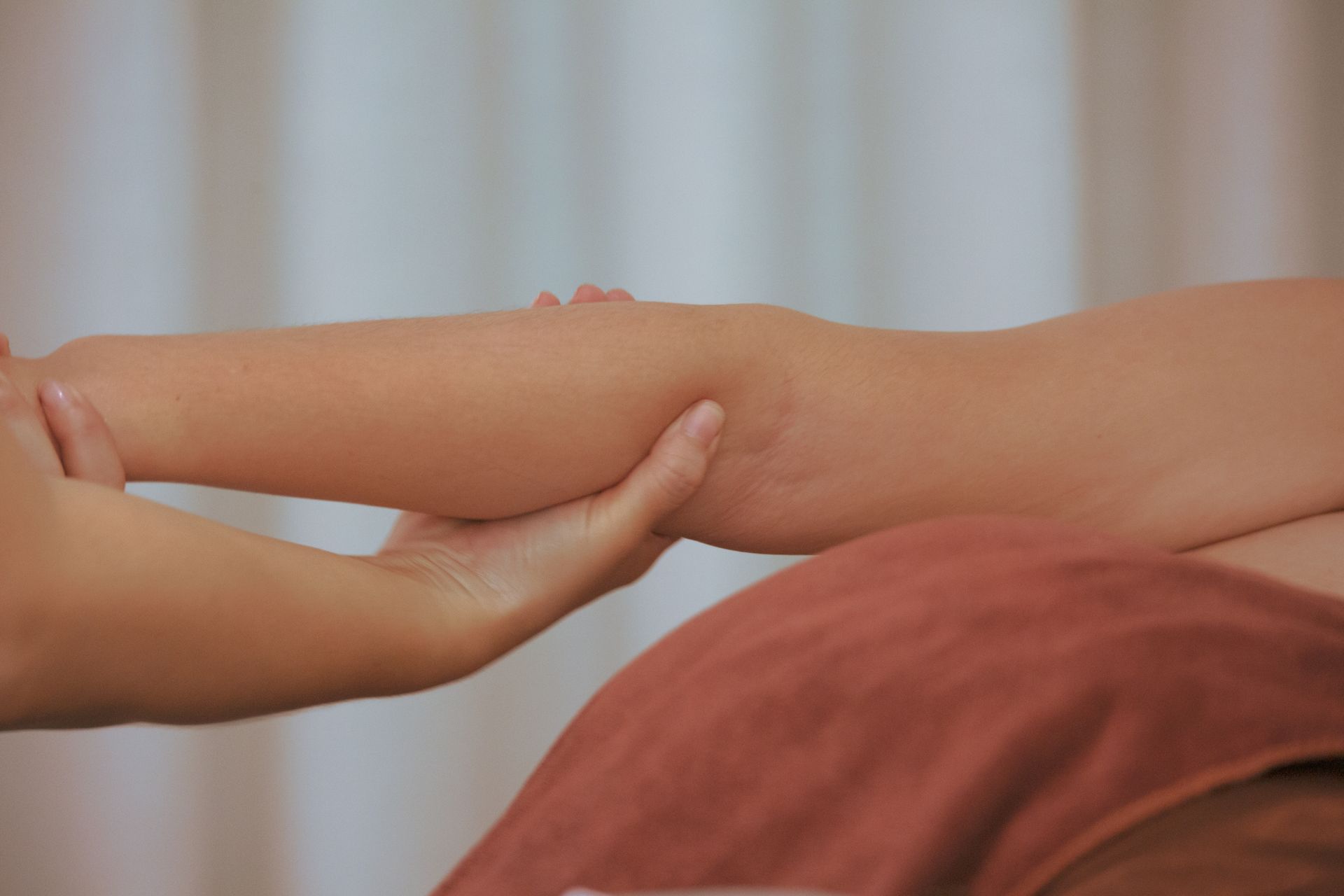 Hände, die während einer Massage den Unterarm einer Person halten; im Vordergrund eine rostfarbene Decke.
