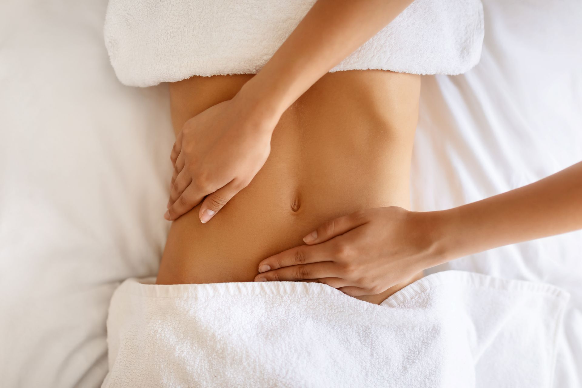 Hände massieren den nackten unteren Rücken einer Person auf einem weißen Bett mit Handtüchern.