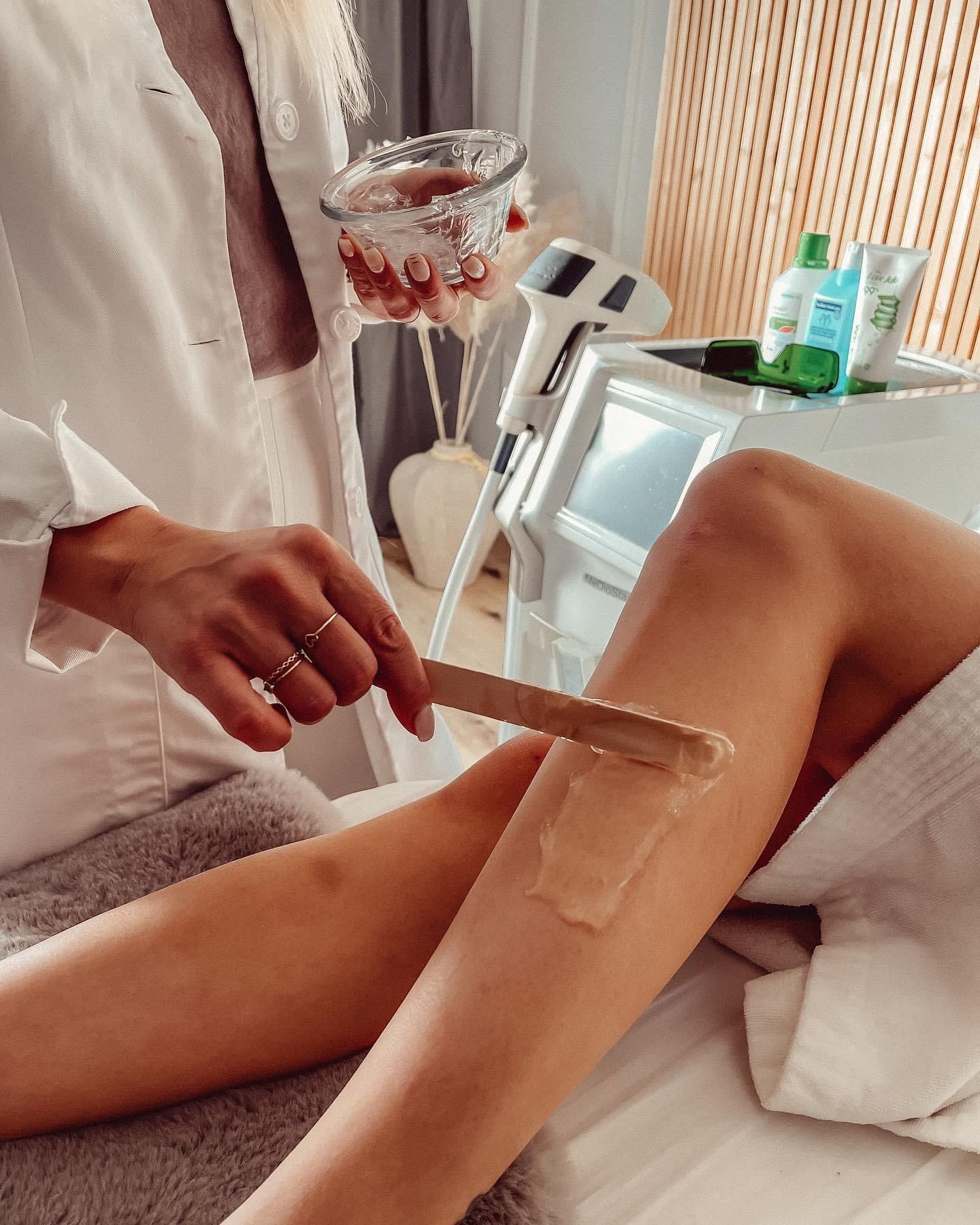 Eine Spa-Therapeutin trägt während einer Beinbehandlung mit einem Spatel Wachs auf das Bein einer Kundin auf.