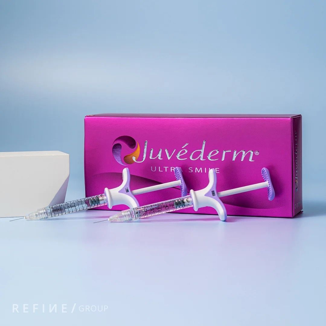 Rosa Juvederm Ultra Smile-Verpackung mit zwei Spritzen auf hellblauem Grund, links daneben ein weißer Block.
