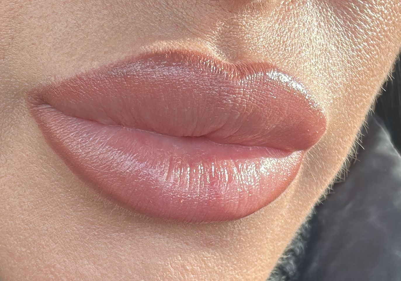 Nahaufnahme von glänzenden, rosafarbenen Lippen mit dezentem Make-up und natürlicher Hautstruktur