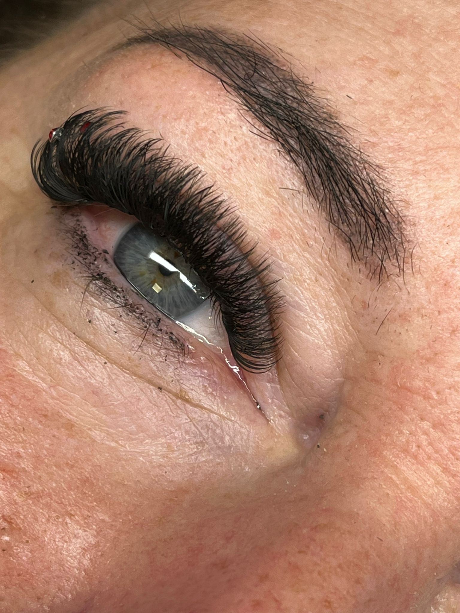 Nahaufnahme eines Auges mit langen schwarzen Wimpern, dunklem Lidschatten und einer formschönen Augenbraue.