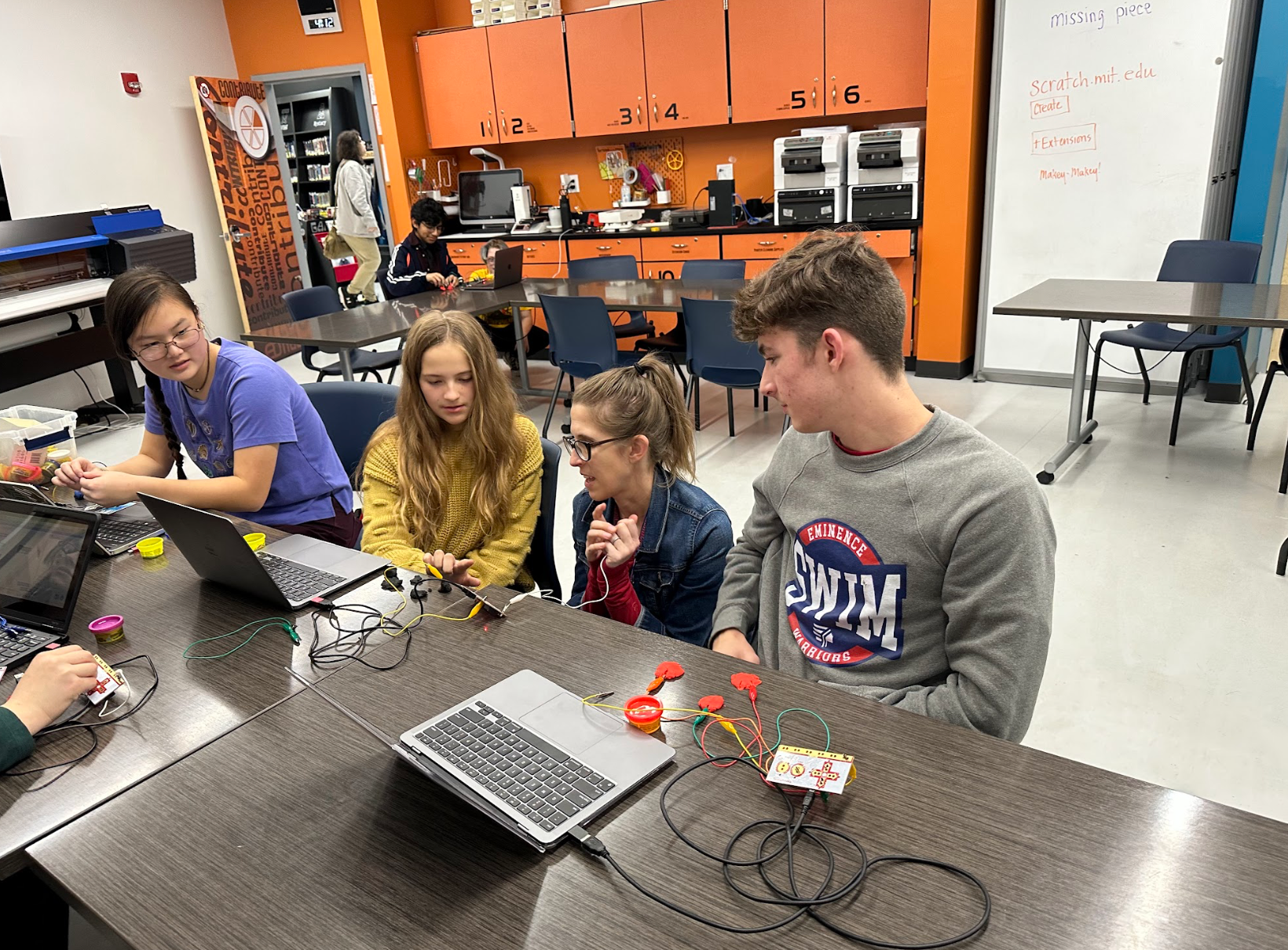 A group of people are sitting around a table with laptops.