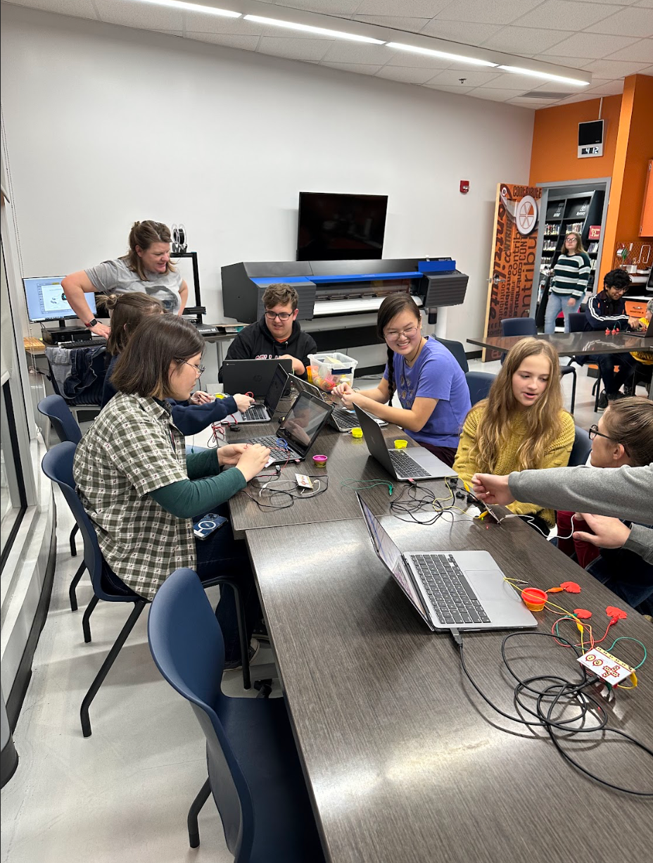 A group of people are sitting around a table with laptops.