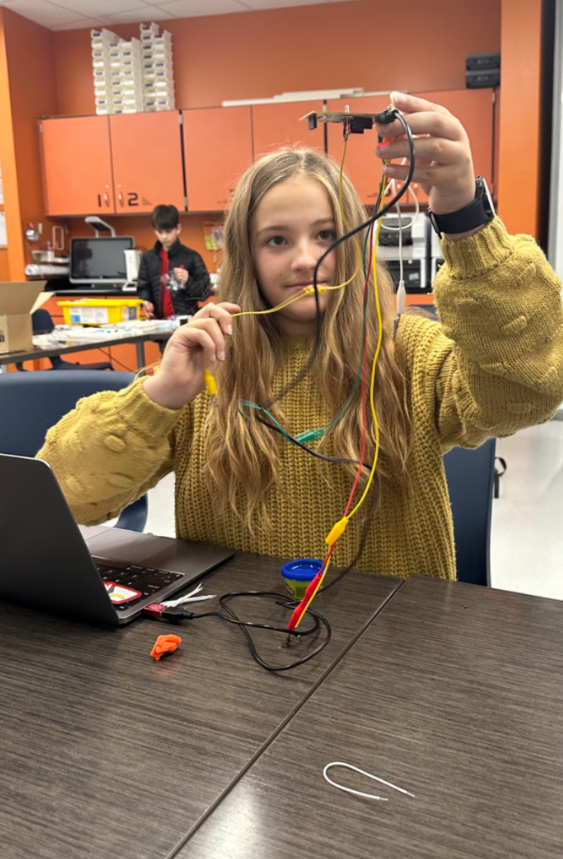 A young girl is sitting at a table holding a piece of wire.