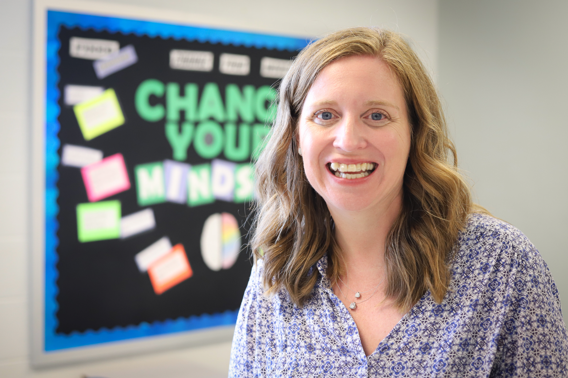 A woman is smiling in front of a bulletin board that says change your minds
