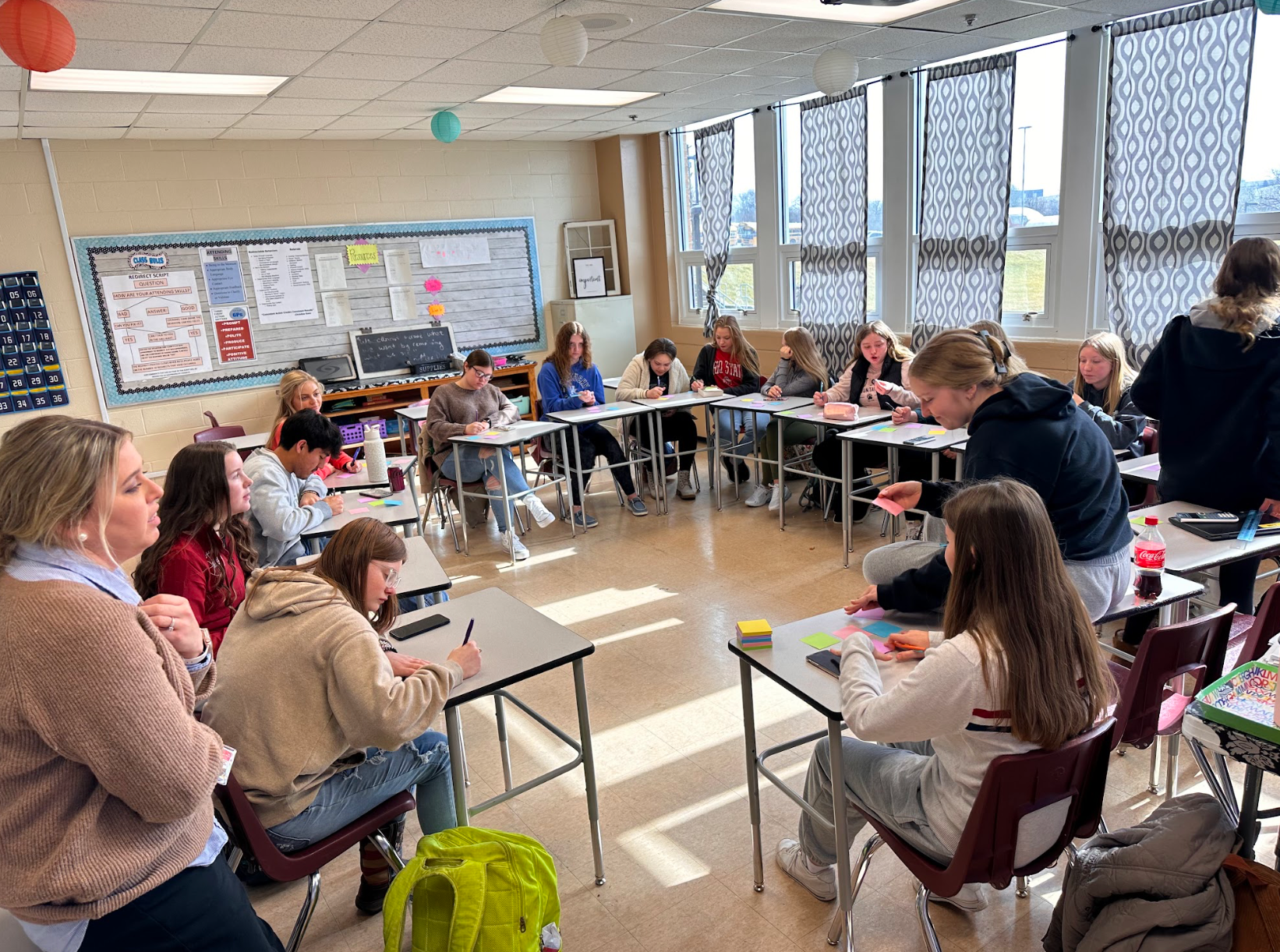 A group of people are sitting at tables in a classroom.
