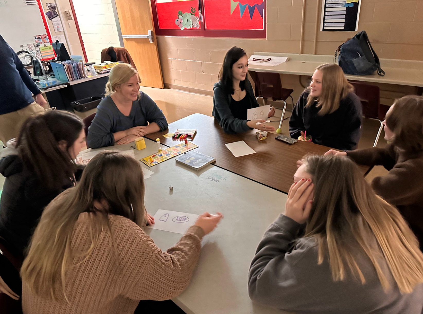 A group of people are sitting around a table in a classroom.