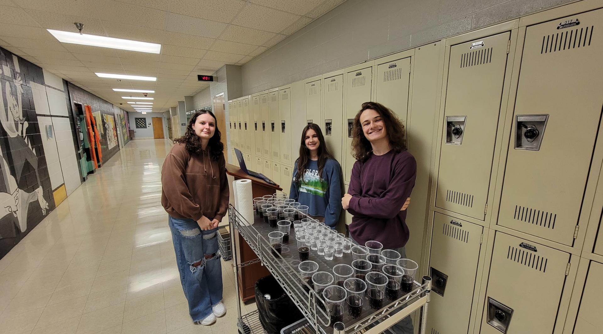 Three women are standing in a hallway next to lockers.