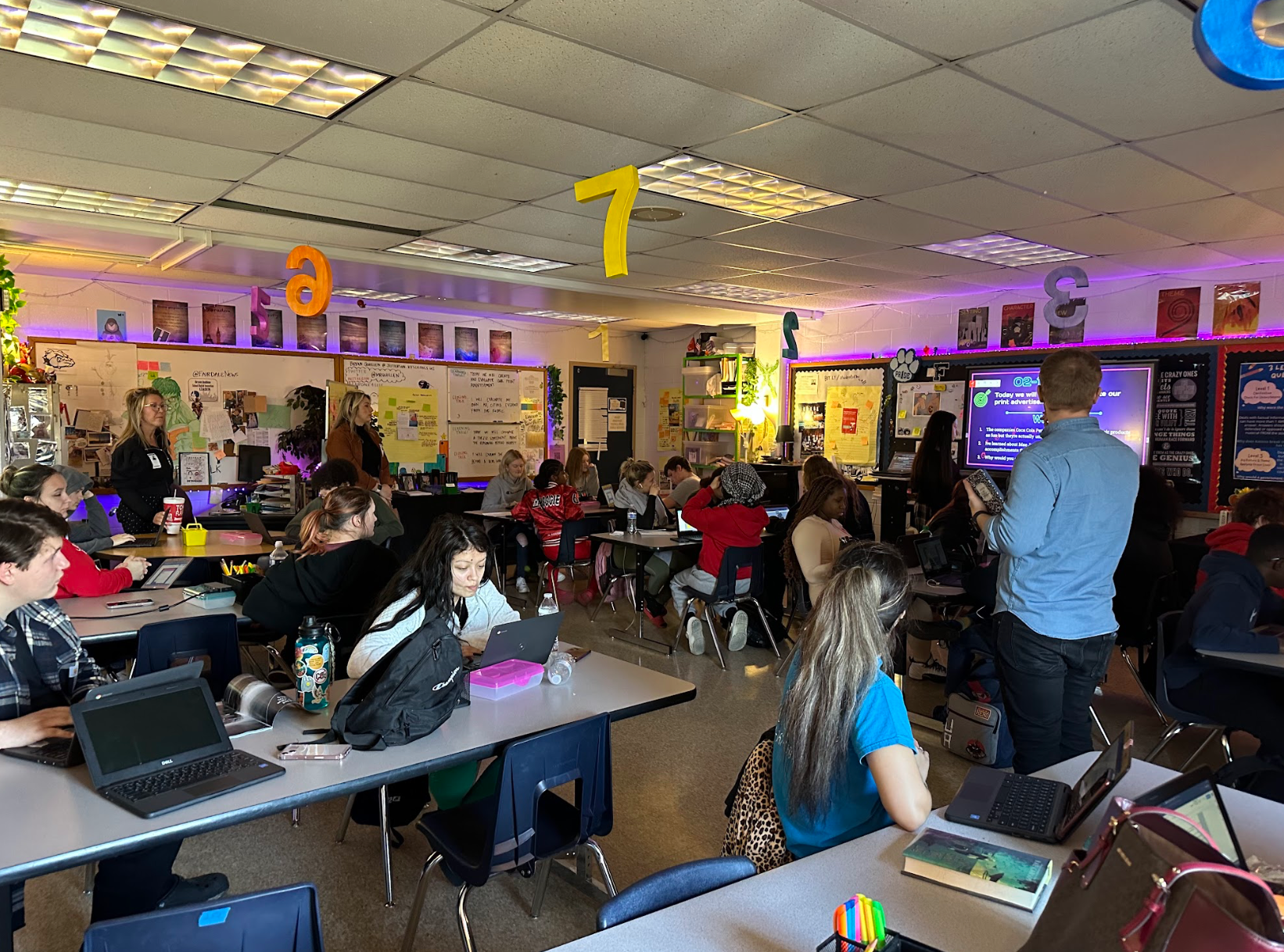 A group of children are sitting at tables in a classroom with laptops.