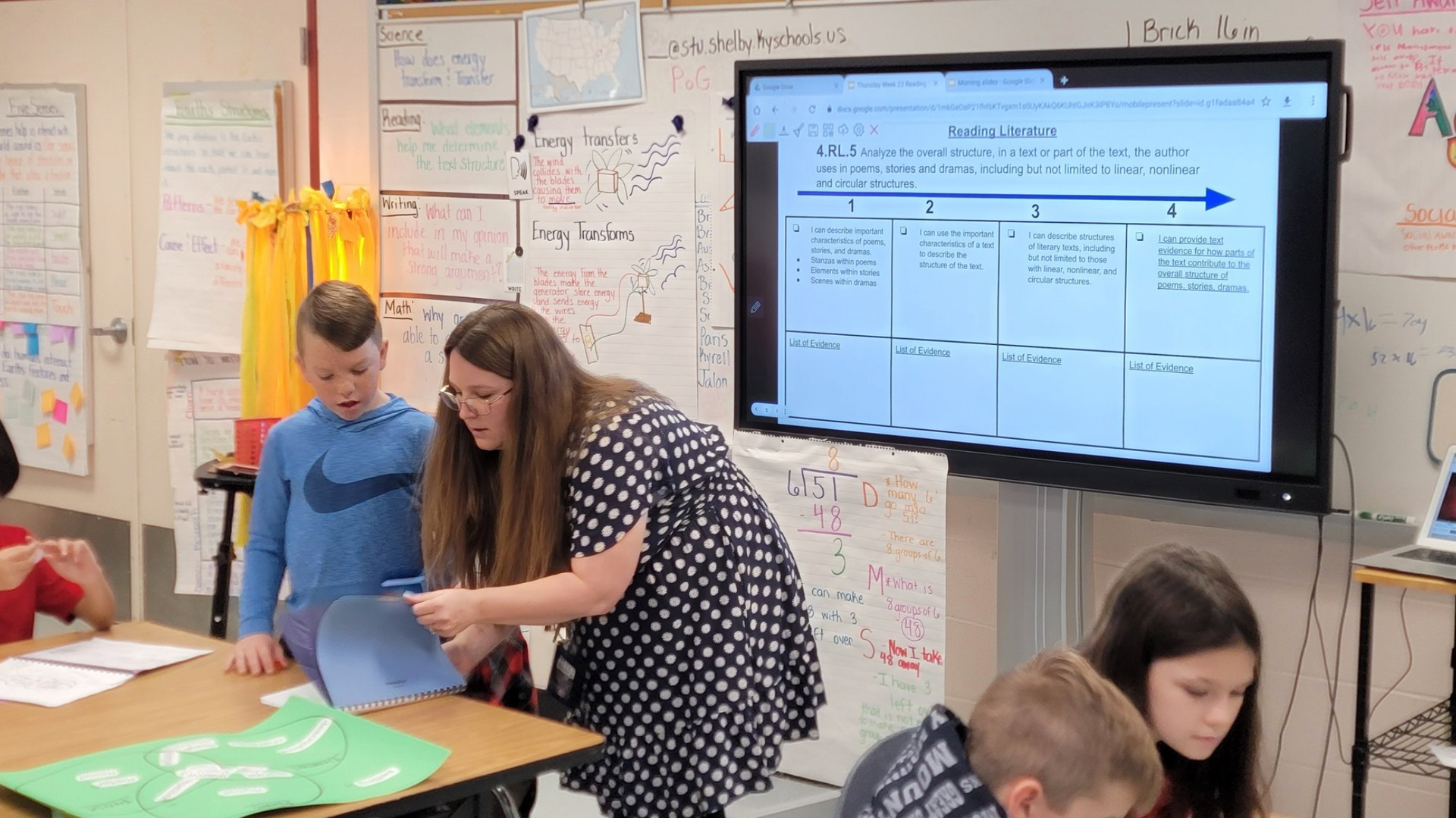 A teacher is helping a student with a projection screen in a classroom.