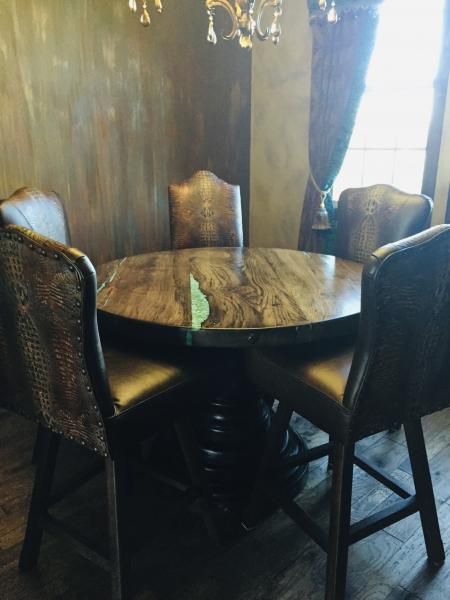 Round wooden table with four upholstered chairs in a dimly lit dining room by a bright window