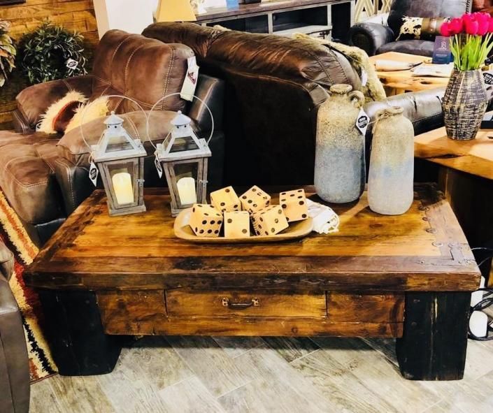 Rustic coffee table with lanterns, dice, jars, pillows, and a fur throw in a cozy living room setting