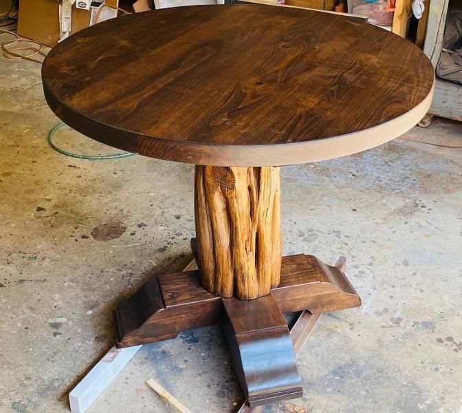 Rustic round wooden table with a live-edge top and carved wooden base on a workshop floor