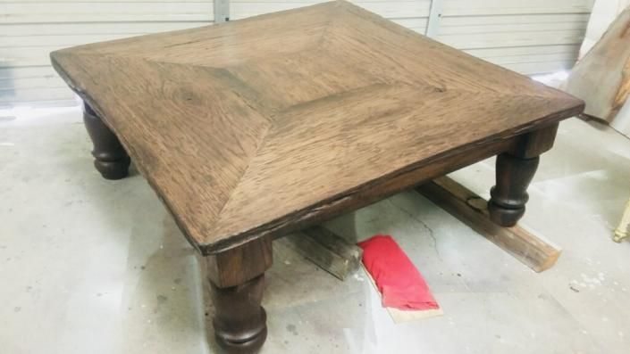 Rustic wooden coffee table with four turned legs in a workshop or garage setting