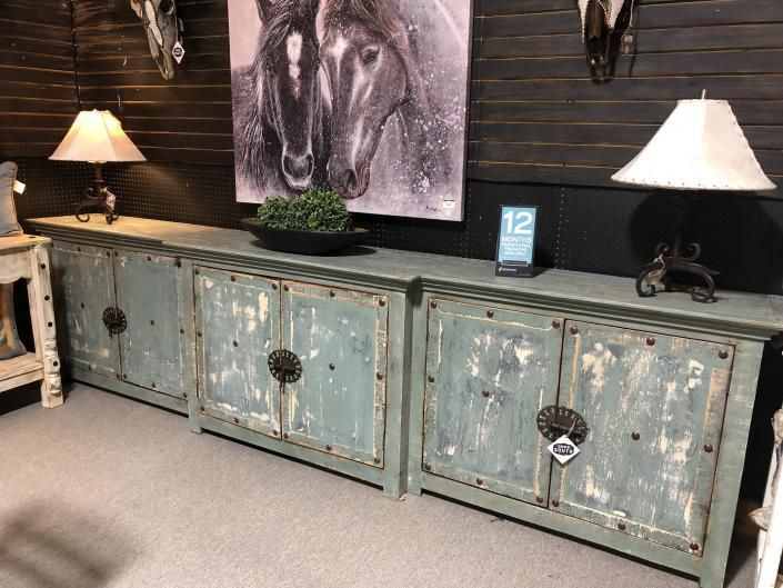 Rustic distressed blue-green sideboard with lamps and horse artwork against a dark wood wall