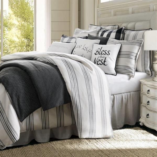 Bright bedroom with a white bed, striped black-and-white bedding, and a “bless this nest” pillow