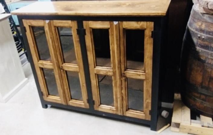 Rustic wood cabinet with glass-paneled doors and a wooden top, next to a barrel on a pallet