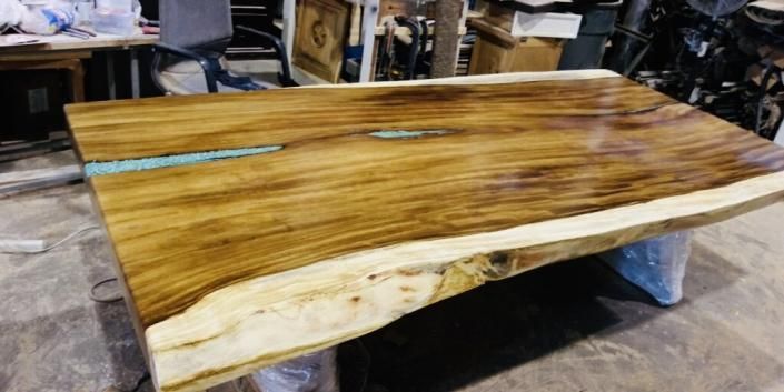 Wooden live-edge tabletop with a glossy finish in a workshop, with a blue pencil on top