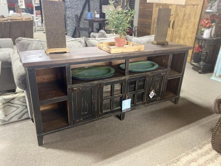 Dark wooden sideboard with open shelves and green decorative trays in an antique shop setting