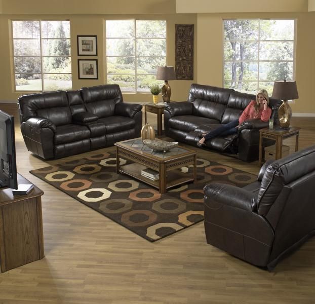 Living room with black leather sofas, patterned rug, coffee table, and a woman seated on the couch