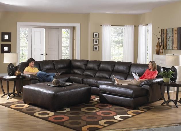 Modern living room with a black sectional, two people seated apart, and large windows with blinds
