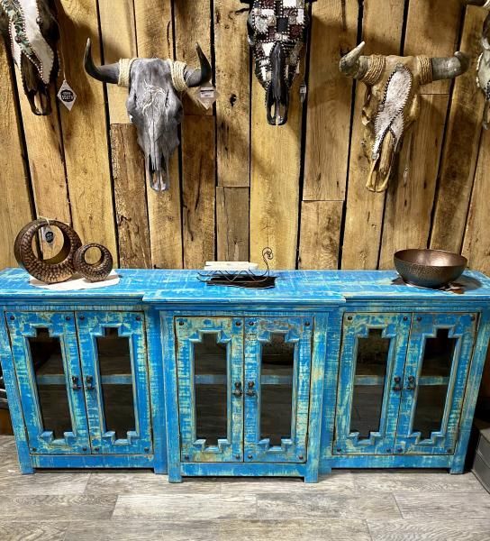 Rustic blue distressed cabinet beneath mounted animal skulls on a wooden wall.