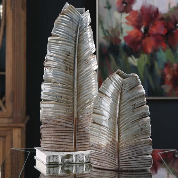 Abstract metallic sculpture with two ribbed, leaf-like towers on a glass surface indoors