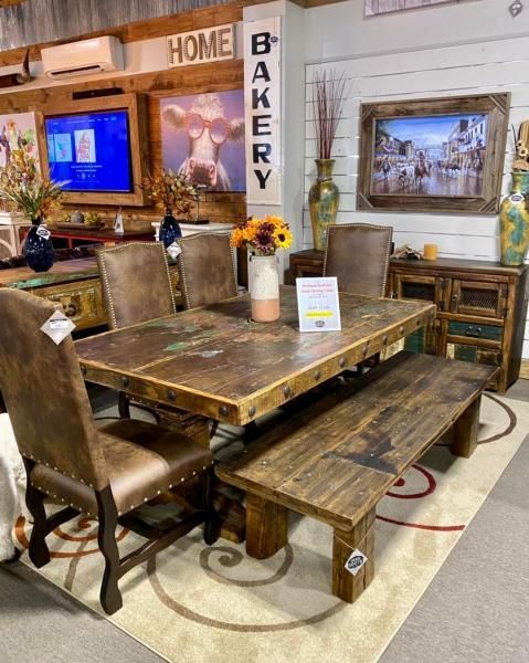 Rustic wooden dining set in a home decor showroom with framed wall art and a bakery sign.