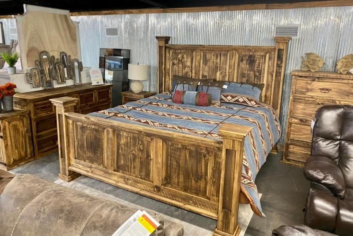 Rustic wooden bedroom with a large bed, dresser, lamp, and leather chair in neutral tones.