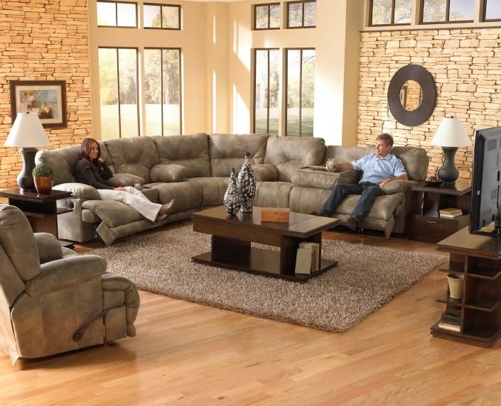 Living room with two people on a sectional sofa, coffee table, armchair, and stone fireplace.