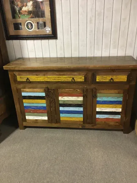 Rustic wooden sideboard with colorful painted drawer and cabinet panels against a paneled wall.