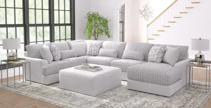 Bright modern living room with a light gray sectional sofa, ottoman, lamps, and staircase