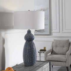 Blue vase on a gray table in a bright living room with a white lamp and beige chair
