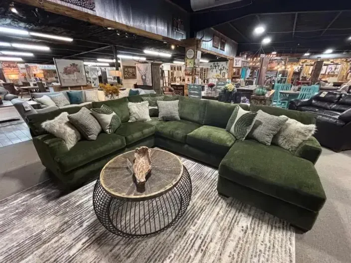 Dark green sectional sofa in a furniture showroom with a round coffee table and patterned rug