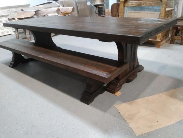 Dark wooden farmhouse-style dining table with attached benches in a workshop or showroom