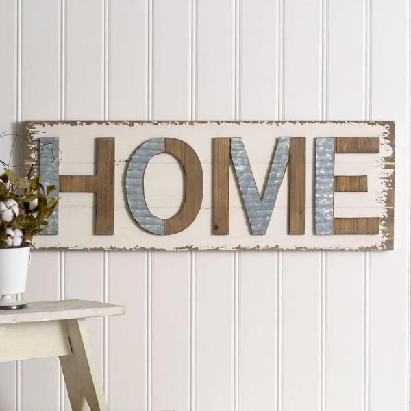 Decorative “HOME” sign in wooden letters on a rustic white wall, beside a small table with a plant