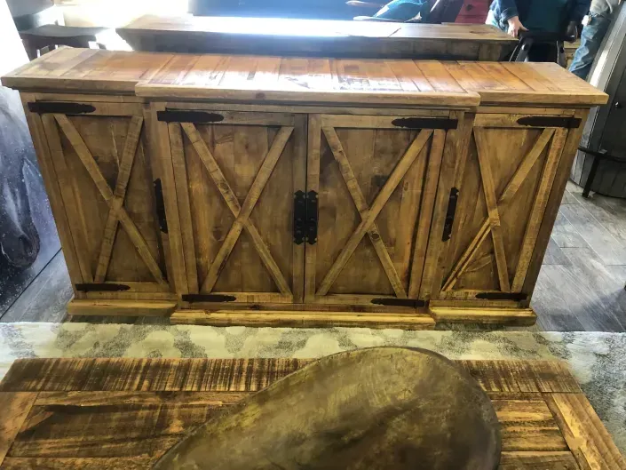 Rustic wooden barn-style console with X-panel doors and a central black handle, on a patterned rug.