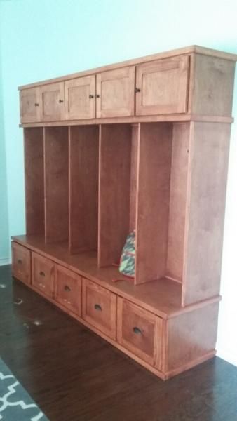 Wooden storage cabinet with open cubbies and drawers in a room with a dark floor.