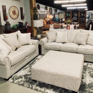 Cream-colored sectional sofa and ottoman on a gray rug in a furniture showroom