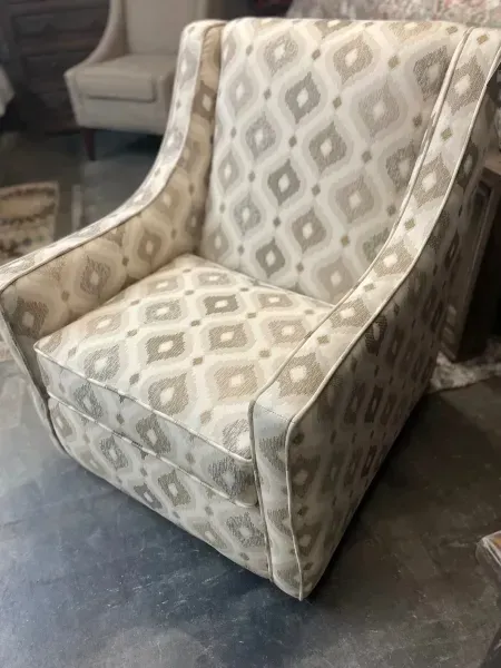 Beige patterned upholstered chair on a dark floor, with a matching sofa in the background