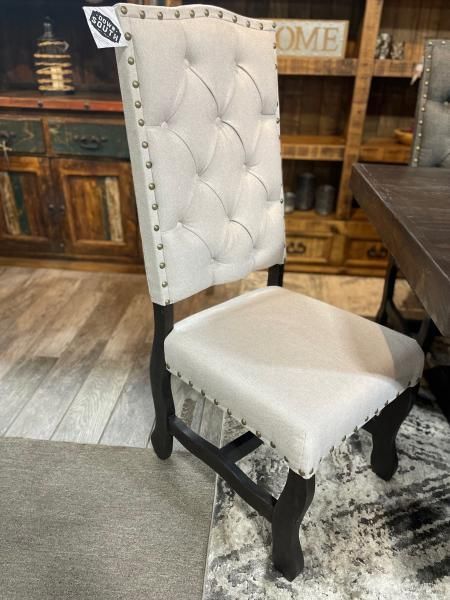 White upholstered tufted dining chair with nailhead trim in a rustic interior setting