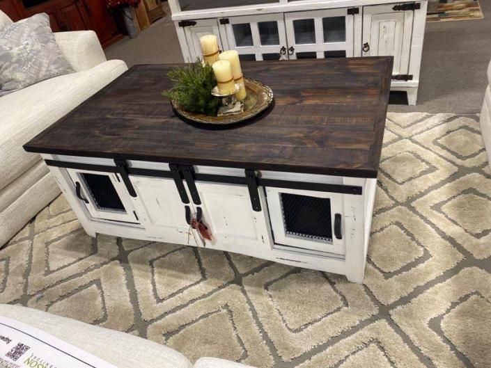 Rustic white storage coffee table with dark wood top in a living room, holding a candle tray.