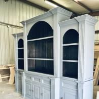 White wooden display cabinet with arched shelving and lower cabinet doors in a workshop