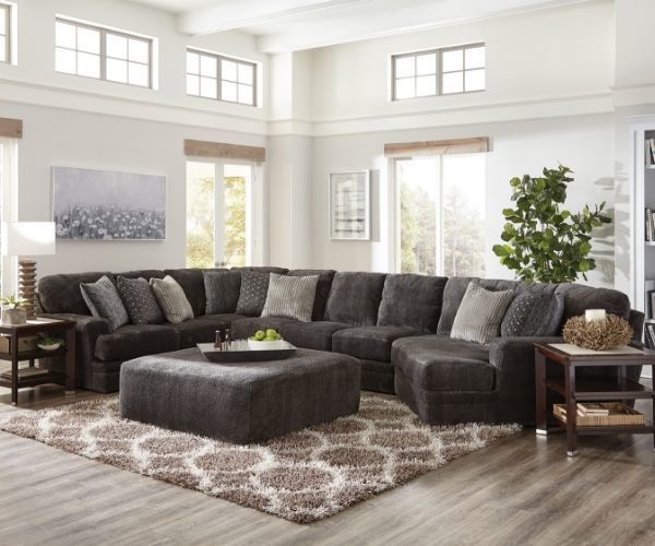 Modern living room with dark sectional sofa, ottoman, patterned rug, and bright windows