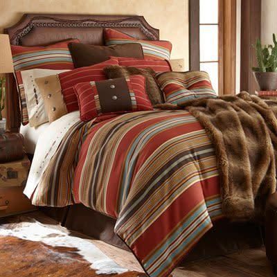 Cozy bed with striped bedding, decorative pillows, and a fur throw in a warmly lit bedroom.