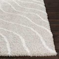 Close-up of a white shaggy rug with subtle wavy pattern on a dark wooden floor