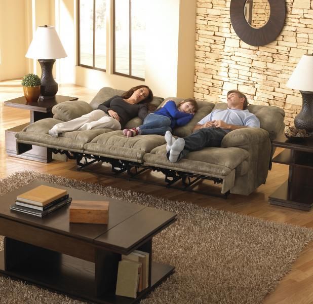 Two people sleeping on a sofa in a cozy living room with stone wall, lamps, and coffee table